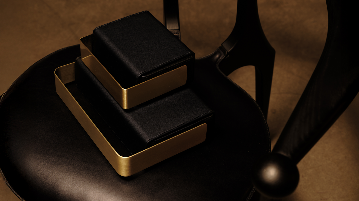 Two black bio-leather BEAM vessels with brushed copper frames stacked on the seat of a sculptural black wooden chair