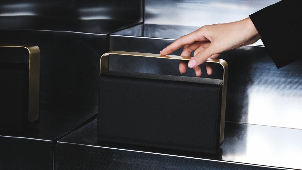 Hand lifting a black bio-leather BEAM vessel by its brushed copper handle from a polished steel step