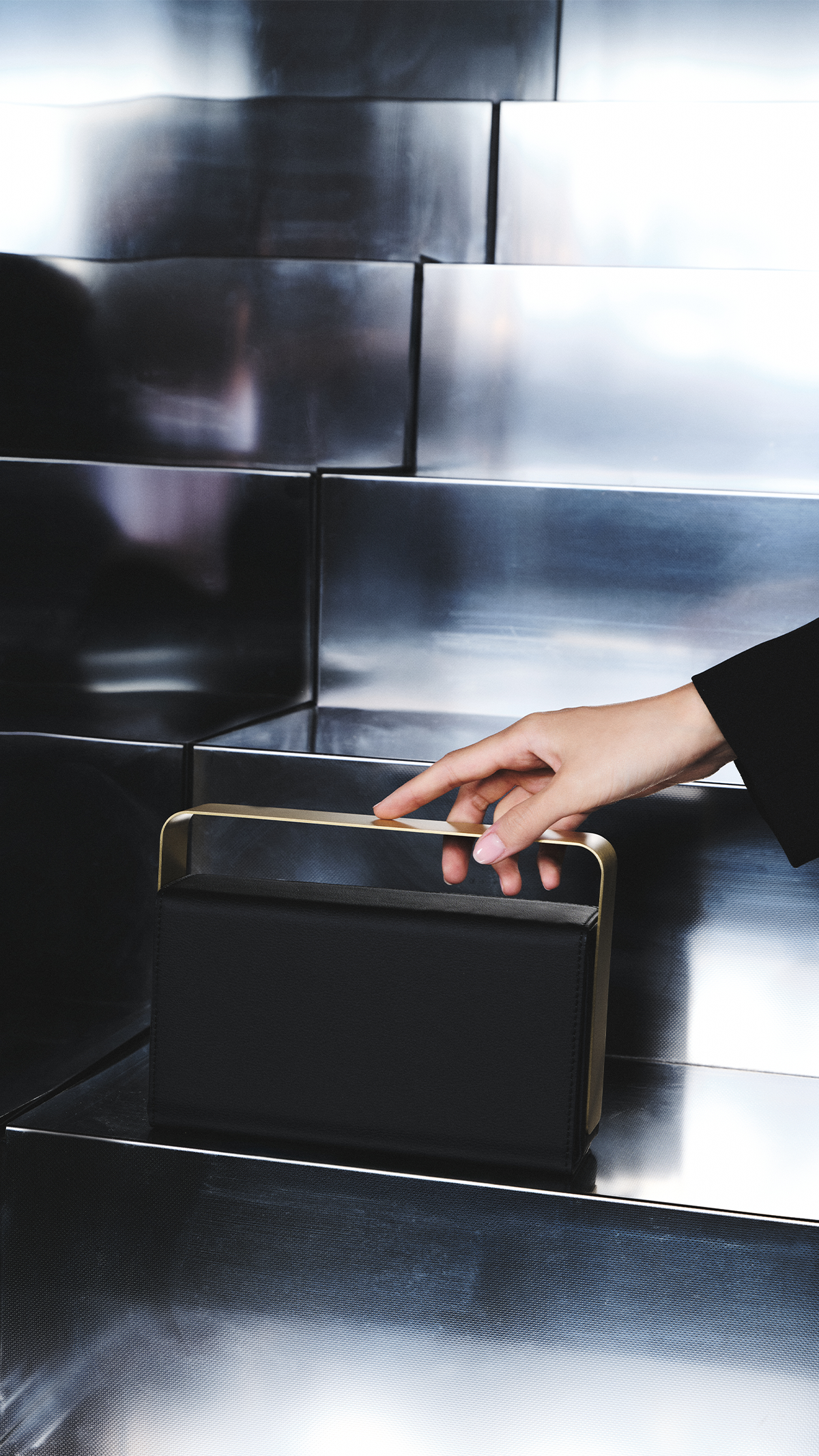 Hand lifting a black bio-leather BEAM vessel by its brushed copper handle from a polished steel step